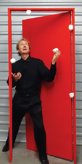 David Cousin standing in a red door way juggling 