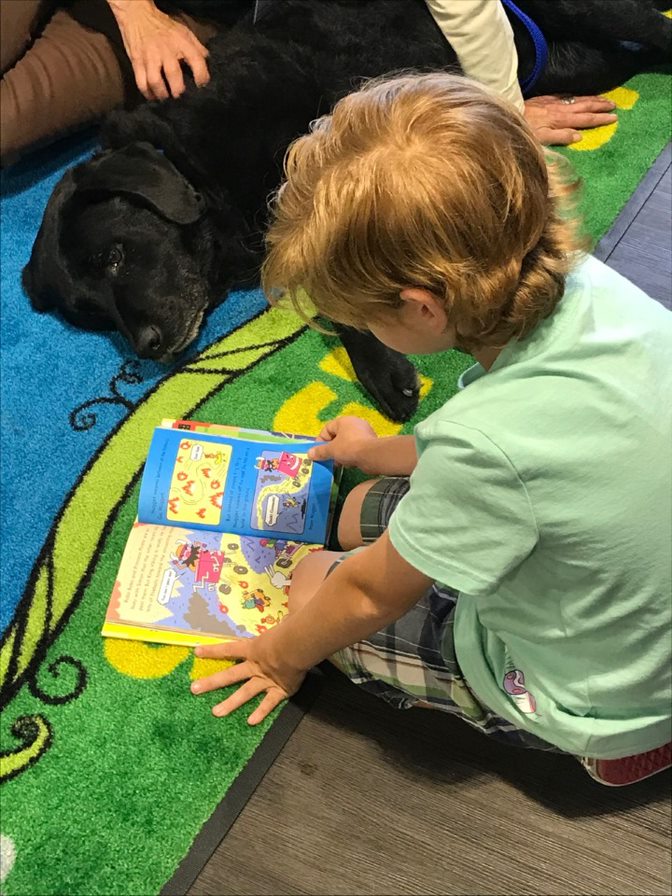 young child reads to a black Labrador Retriever