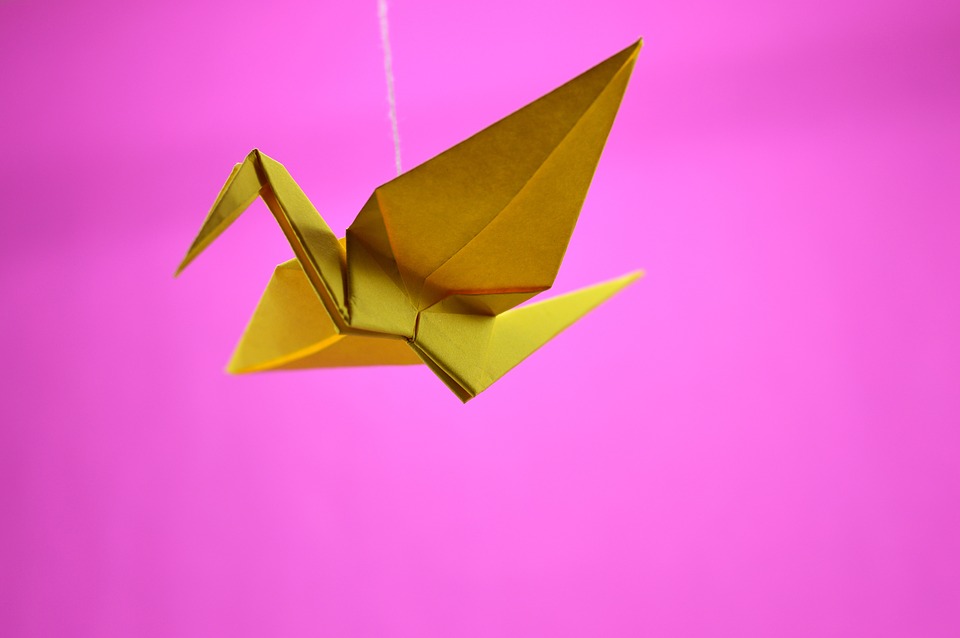 yellow crane origami against a pink background