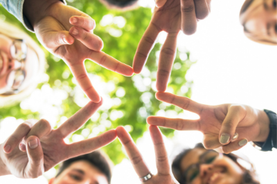 Upshot photo of five teens outdoors in a circle forming with each person displaying the "v" peace sign to form a single communal star.