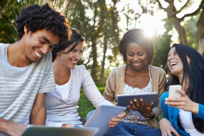 Photo of teens reading outdoors using tablets.