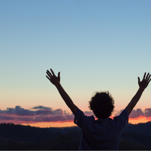 Man facing away from camera with outstretched arms facing the sunset
