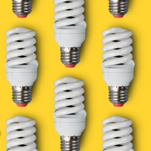 Energy saving spiral lightbulbs place in a pattern on top of a bright yellow background.