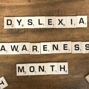 scrabble tiles spell out Dyslexia Awareness Month against a wood background